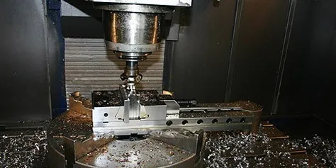 Fräskopf eines CNC-Bearbeitungszentrums über einem eingespannten Werkstück, Späne auf dem Maschinentisch